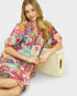 Woman in a colorful dress sitting on a wooden block against a white background