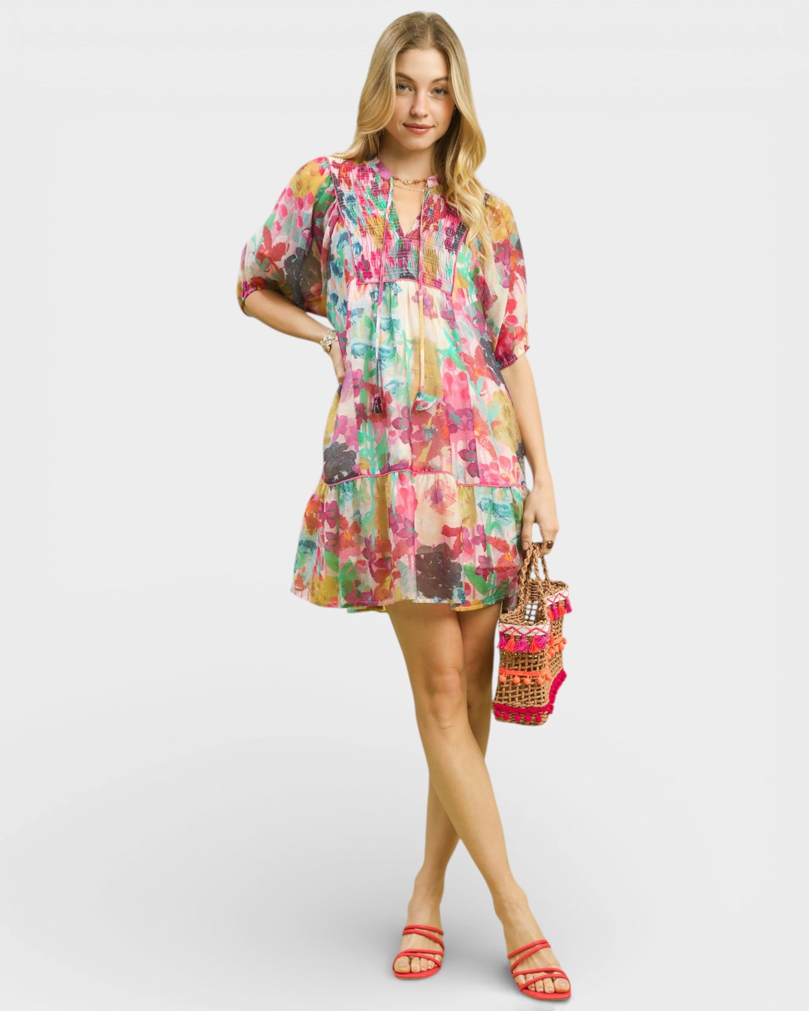 Woman wearing a colorful floral dress holding a woven bag on a white background