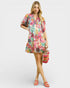 Woman wearing a colorful floral dress holding a woven bag on a white background
