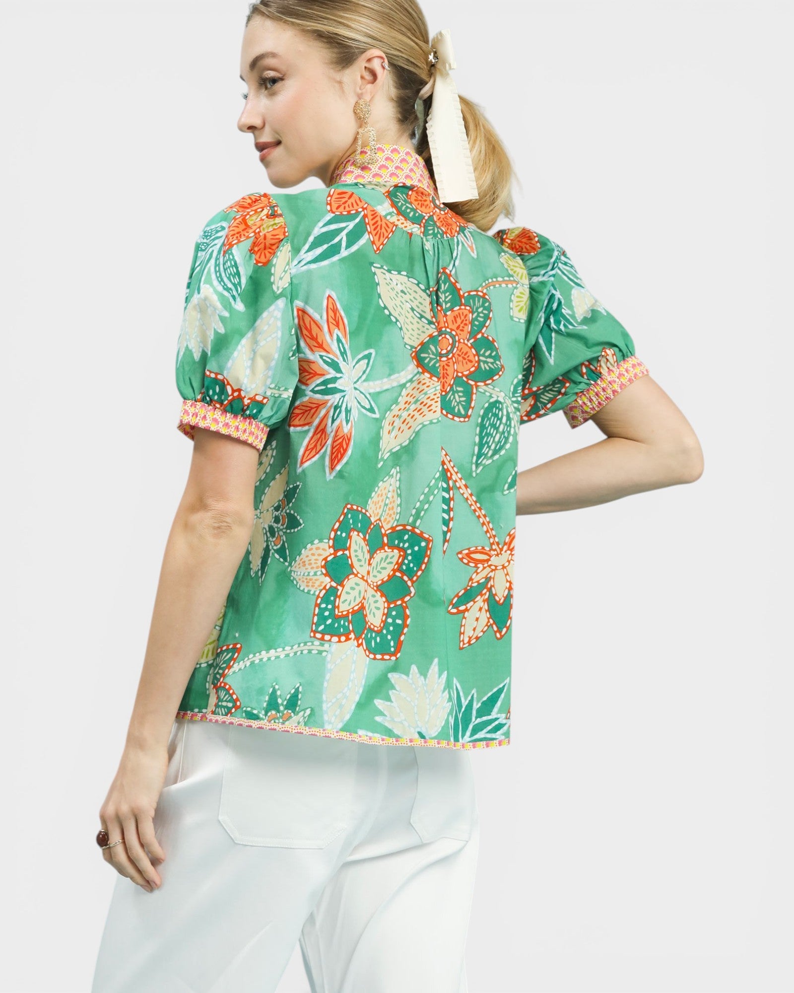 Woman wearing a green floral blouse with white pants on a light gray background