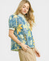 Woman wearing a blue floral blouse with beige pants on a white background