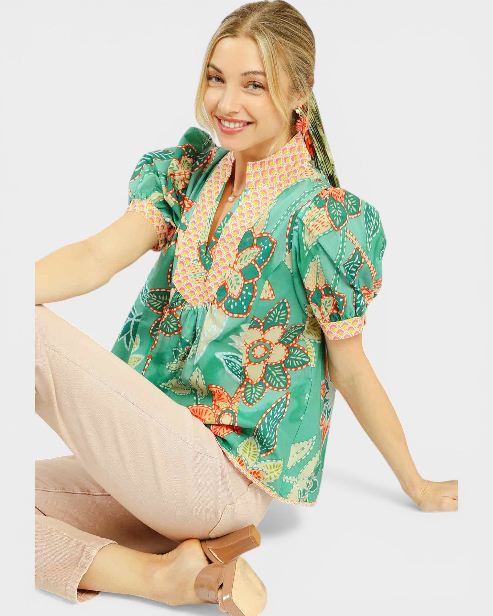 Woman wearing a green floral blouse sitting on a white background