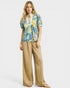 Woman wearing a colorful floral blouse and beige pants on a white background