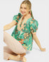 Woman wearing a green floral blouse sitting on a white background