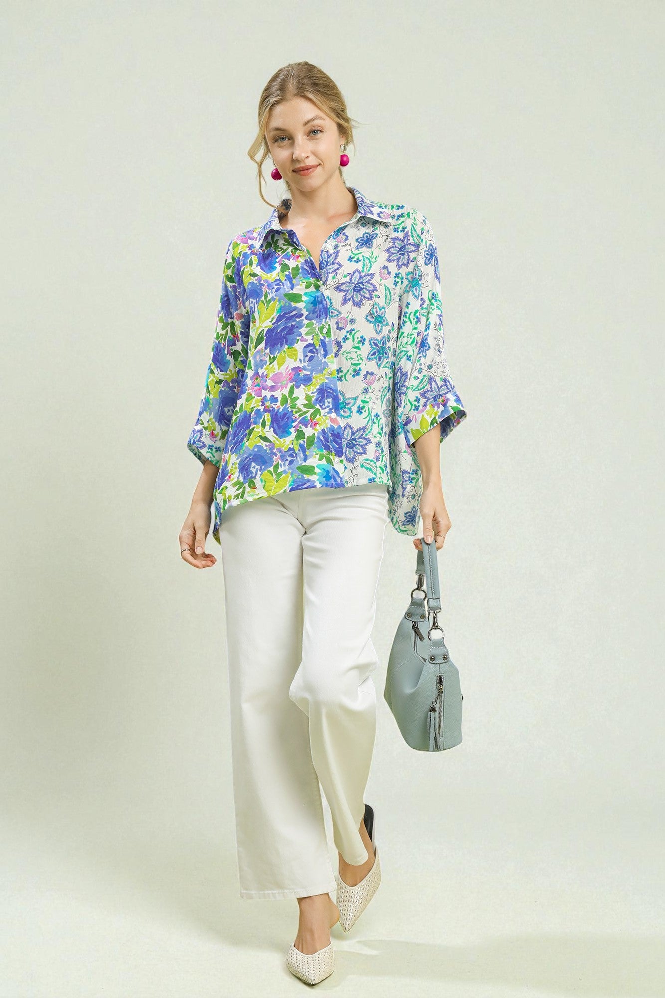 Woman wearing a colorful floral blouse and white pants, holding a gray bag on a white background