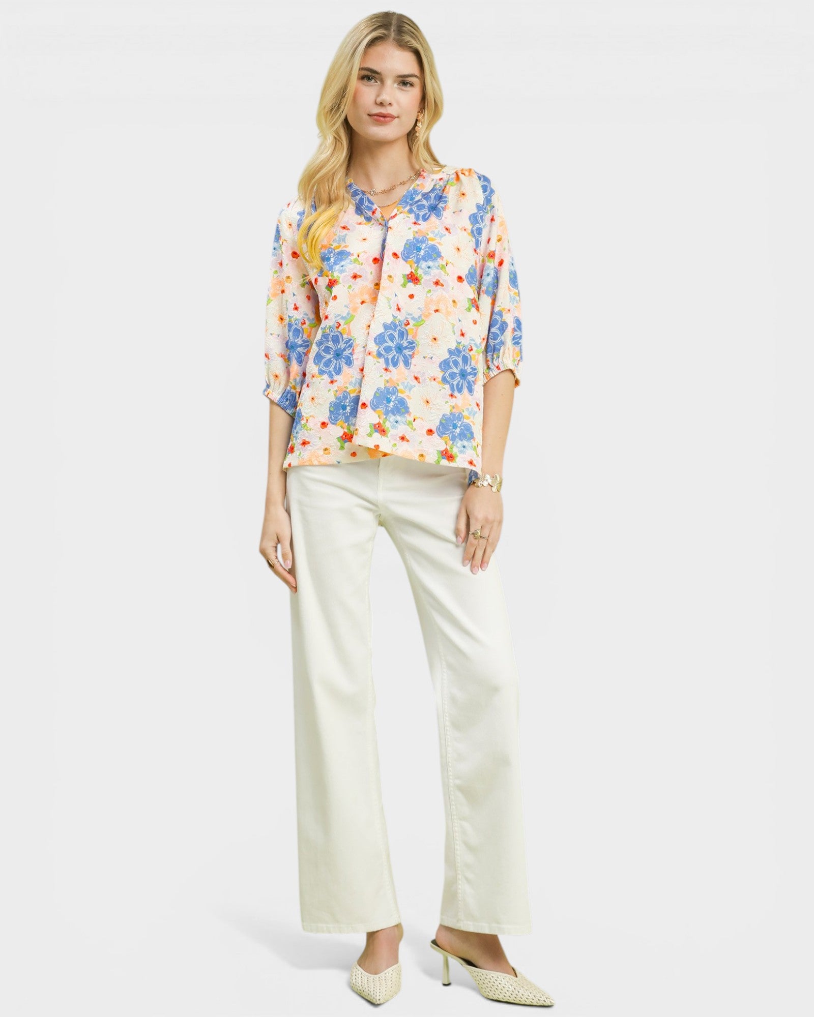 Woman wearing a floral blouse and white pants on a white background