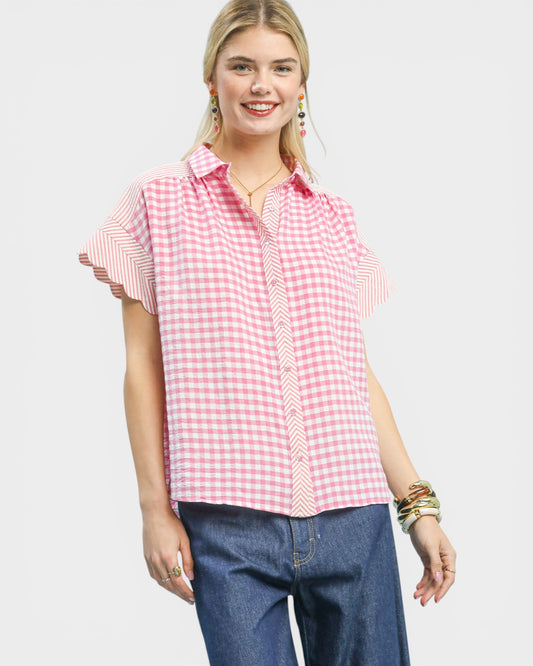 Woman wearing a pink and white checkered shirt with blue jeans on a light gray background