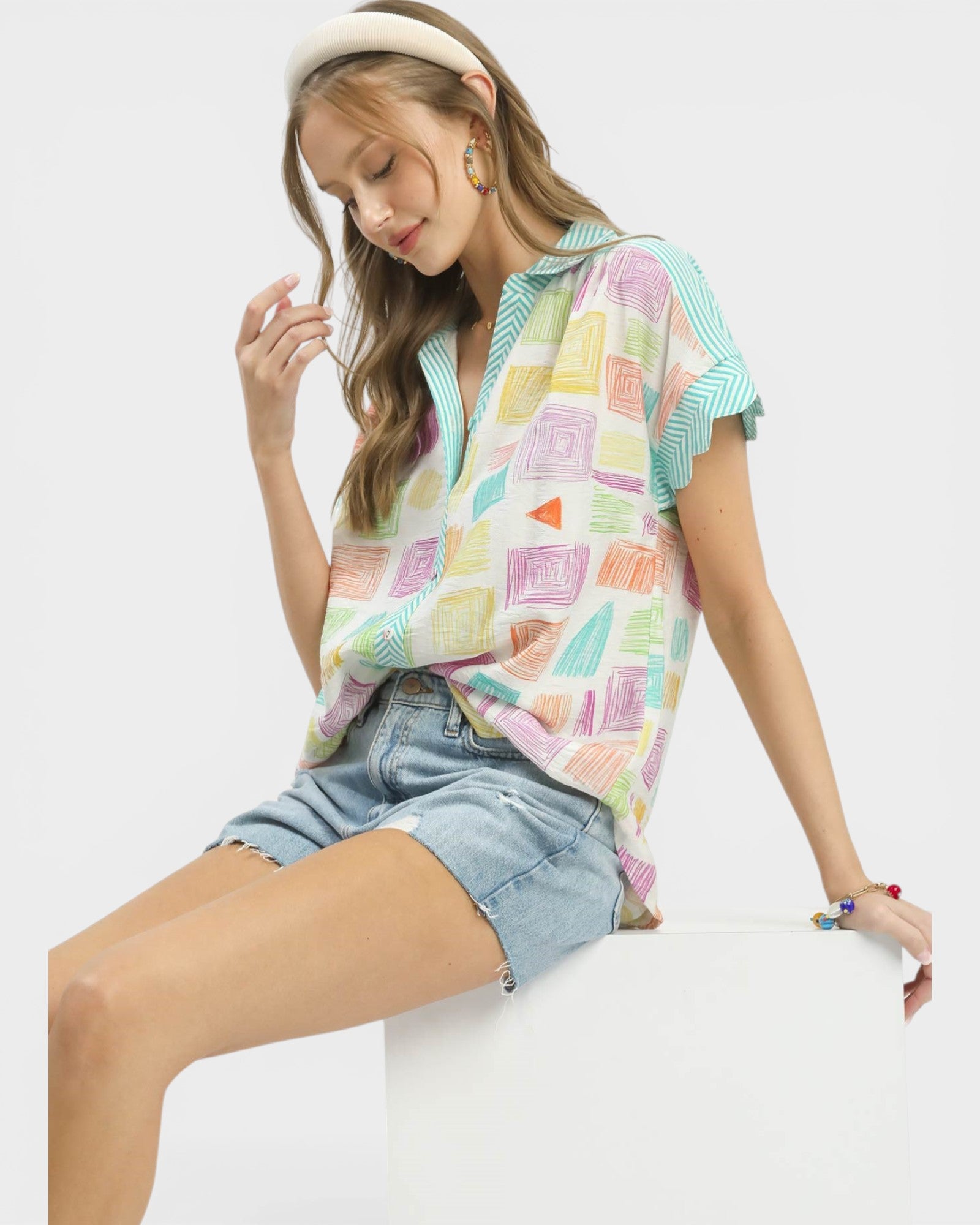 Woman wearing a colorful patterned top and denim shorts on a white background