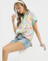 Woman wearing a colorful patterned top and denim shorts on a white background