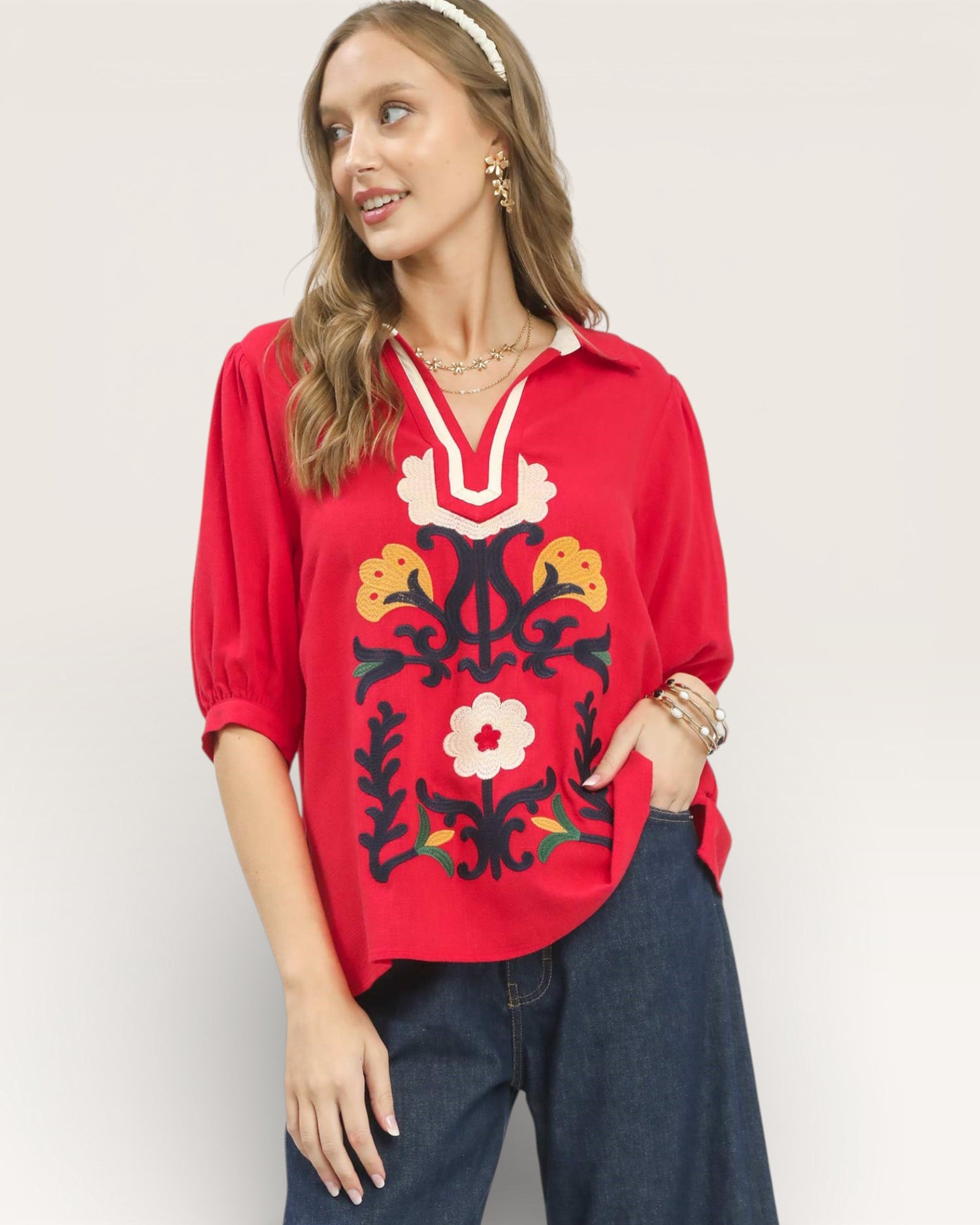 Woman wearing a red blouse with floral embroidery on a plain background