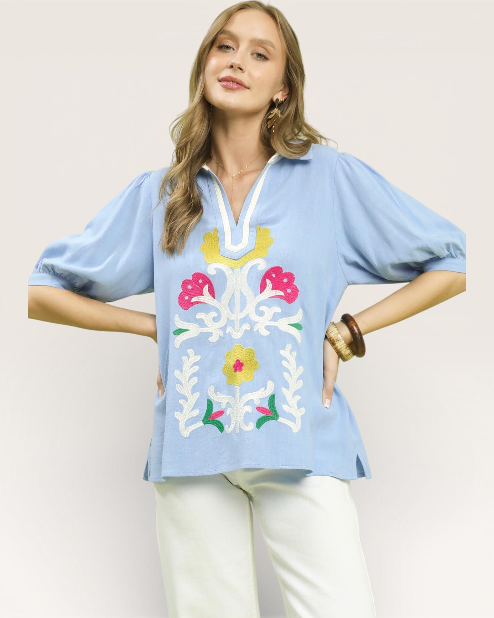 Woman wearing a light blue blouse with colorful floral embroidery on a plain background