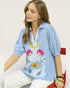 Woman wearing a light blue blouse with colorful floral embroidery on a white background