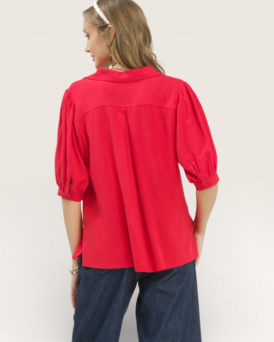 Person wearing a red blouse with puffed sleeves on a plain background