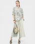 Woman wearing a floral blouse and wide-leg pants holding a woven bag on a white background