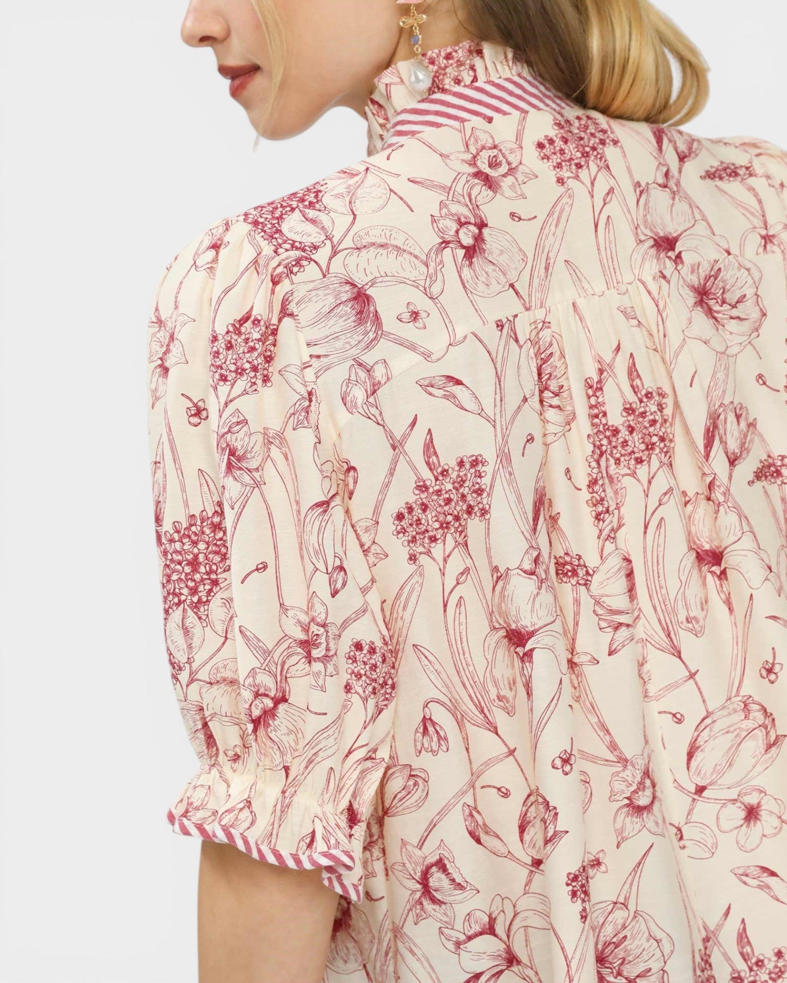 Person wearing a floral patterned blouse with red and pink flowers on a light background