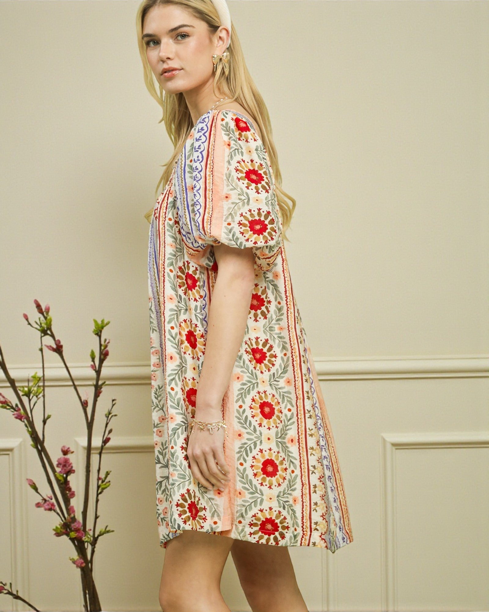 Woman wearing a floral dress standing against a neutral wall with decorative elements.