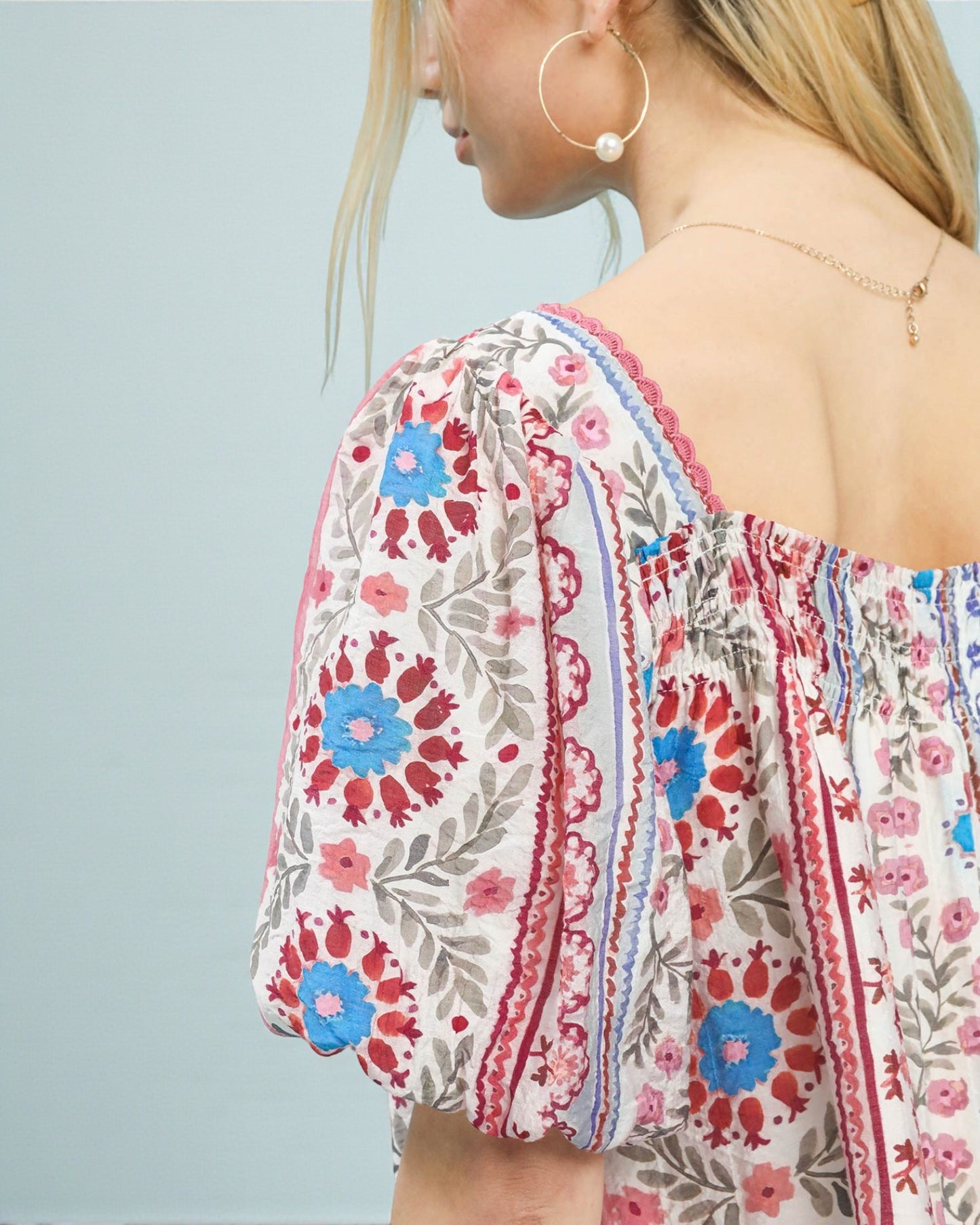 Close-up of a person wearing a floral patterned top with a light blue background