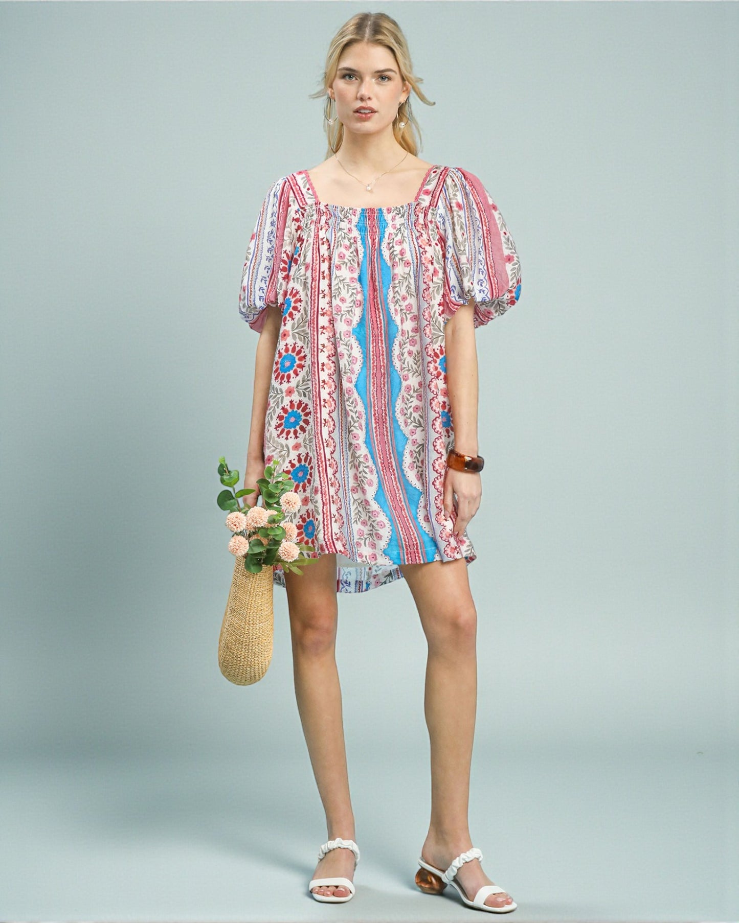 Woman wearing a colorful patterned dress holding flowers against a light gray background