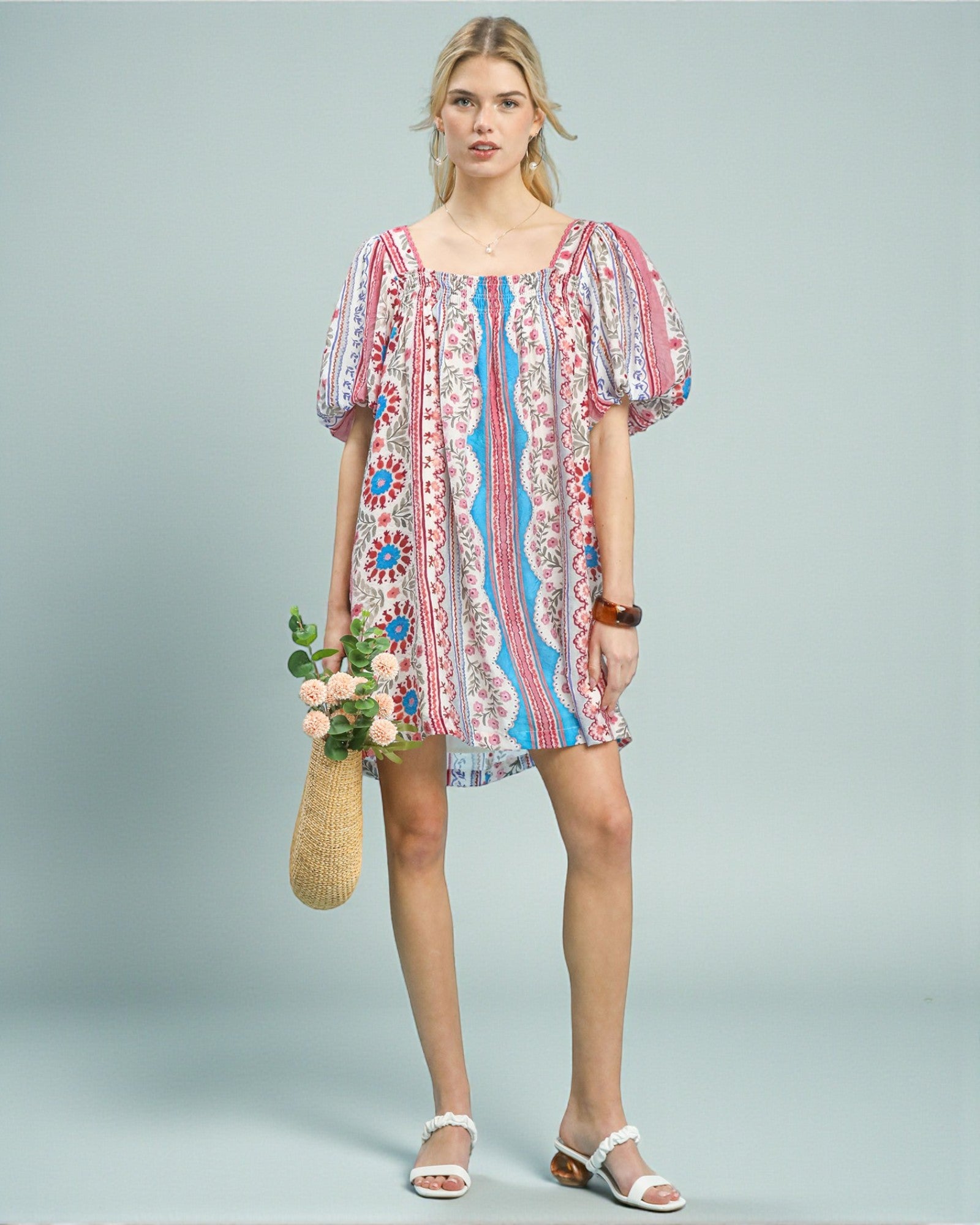 Woman wearing a colorful patterned dress holding flowers against a light gray background