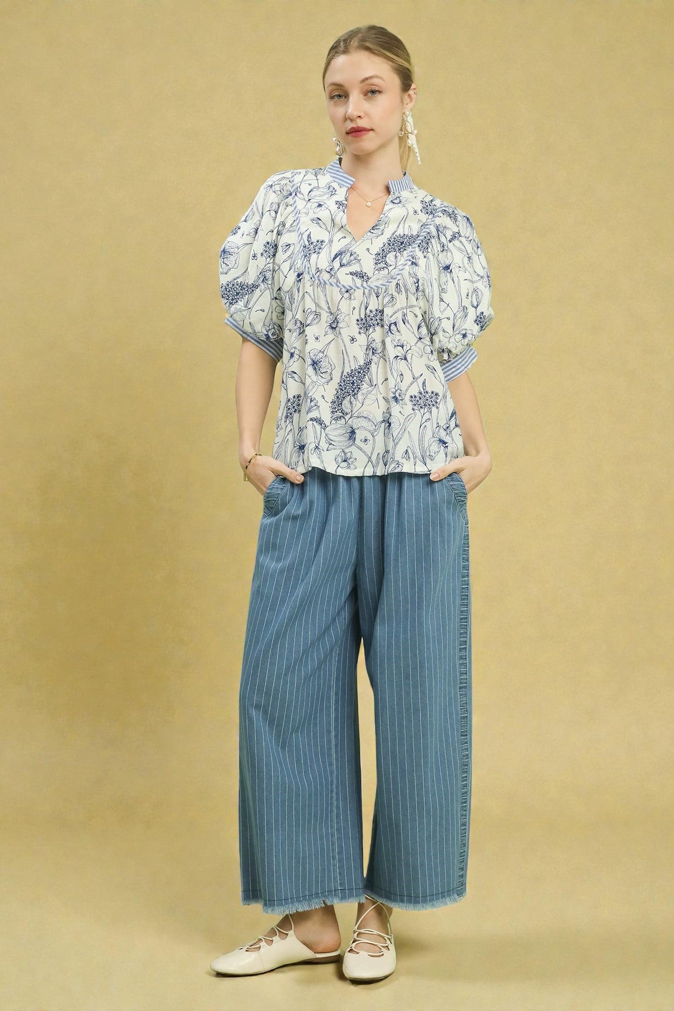 Woman wearing a patterned blouse and blue striped pants on a beige background