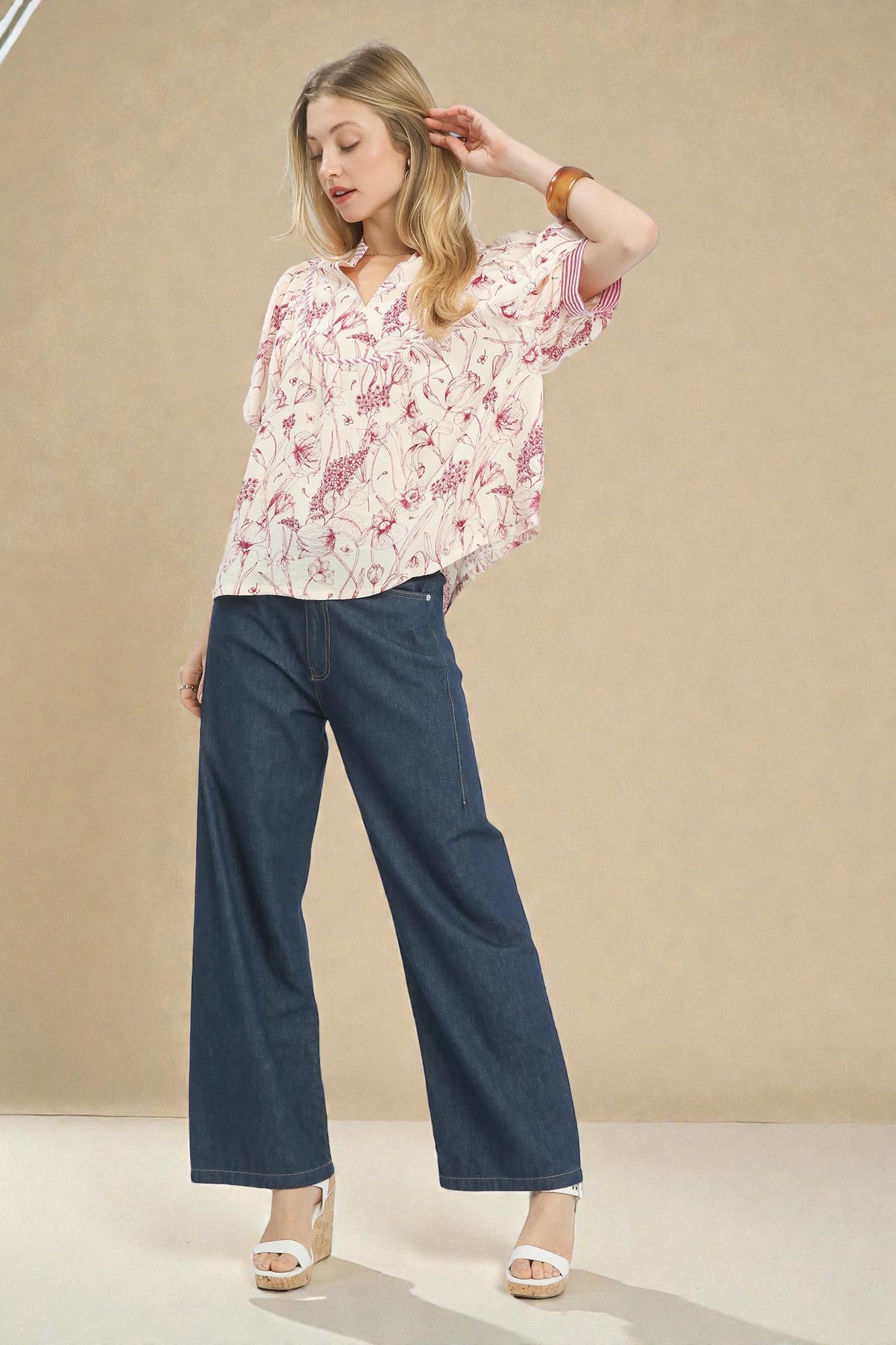 Woman wearing a floral blouse and blue jeans against a beige background