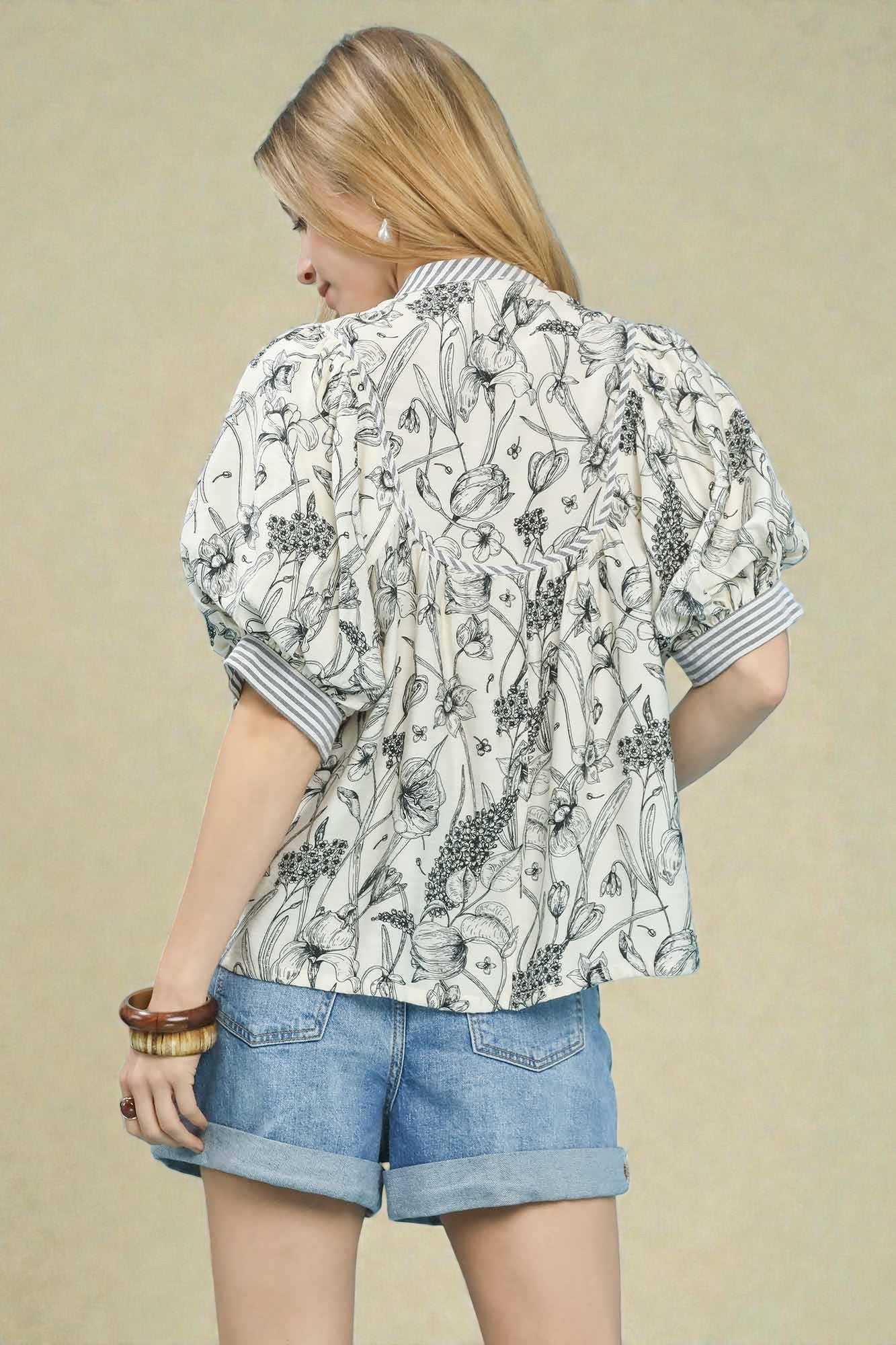 Woman wearing a patterned blouse and denim shorts on a beige background