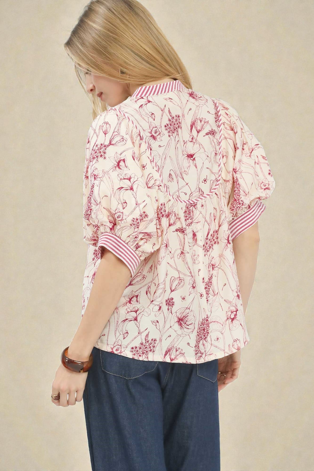 Woman wearing a floral blouse with rolled-up sleeves on a beige background