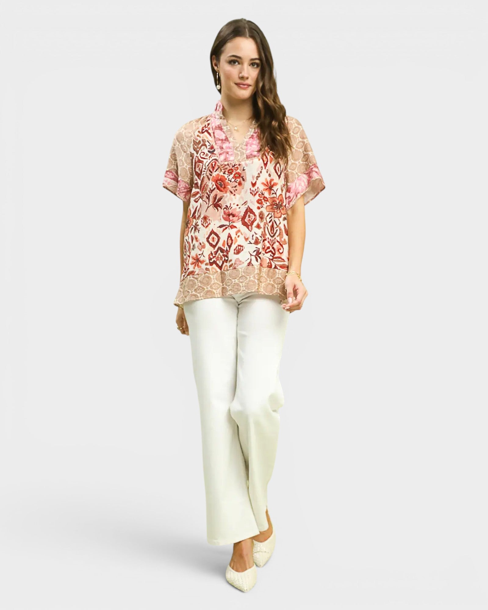 Woman wearing a floral blouse and white pants on a light gray background