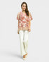 Woman wearing a floral blouse and white pants on a light gray background
