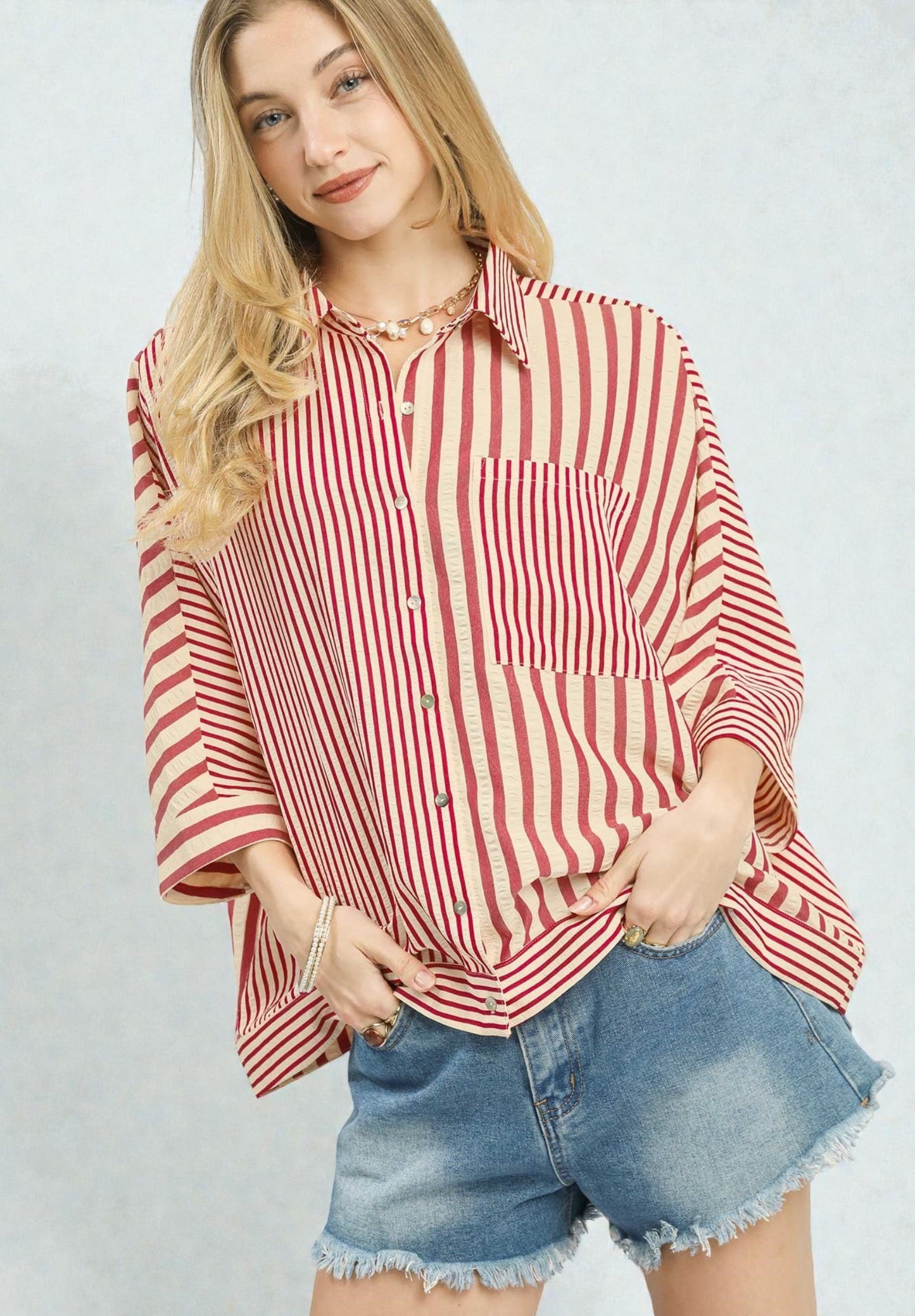 Woman wearing a red and white striped shirt and denim shorts on a plain background