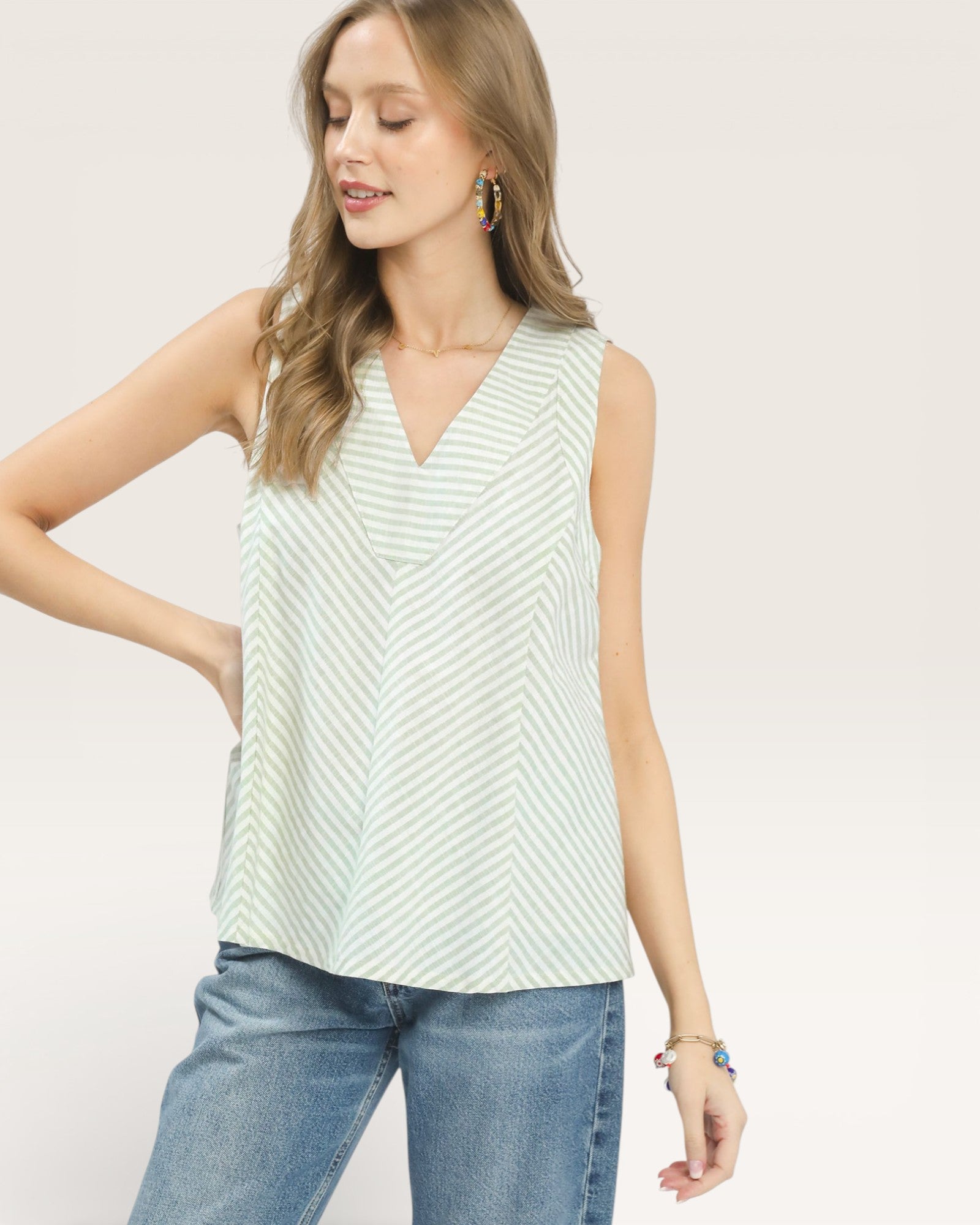 Woman wearing a sleeveless green and white striped top with blue jeans on a plain background
