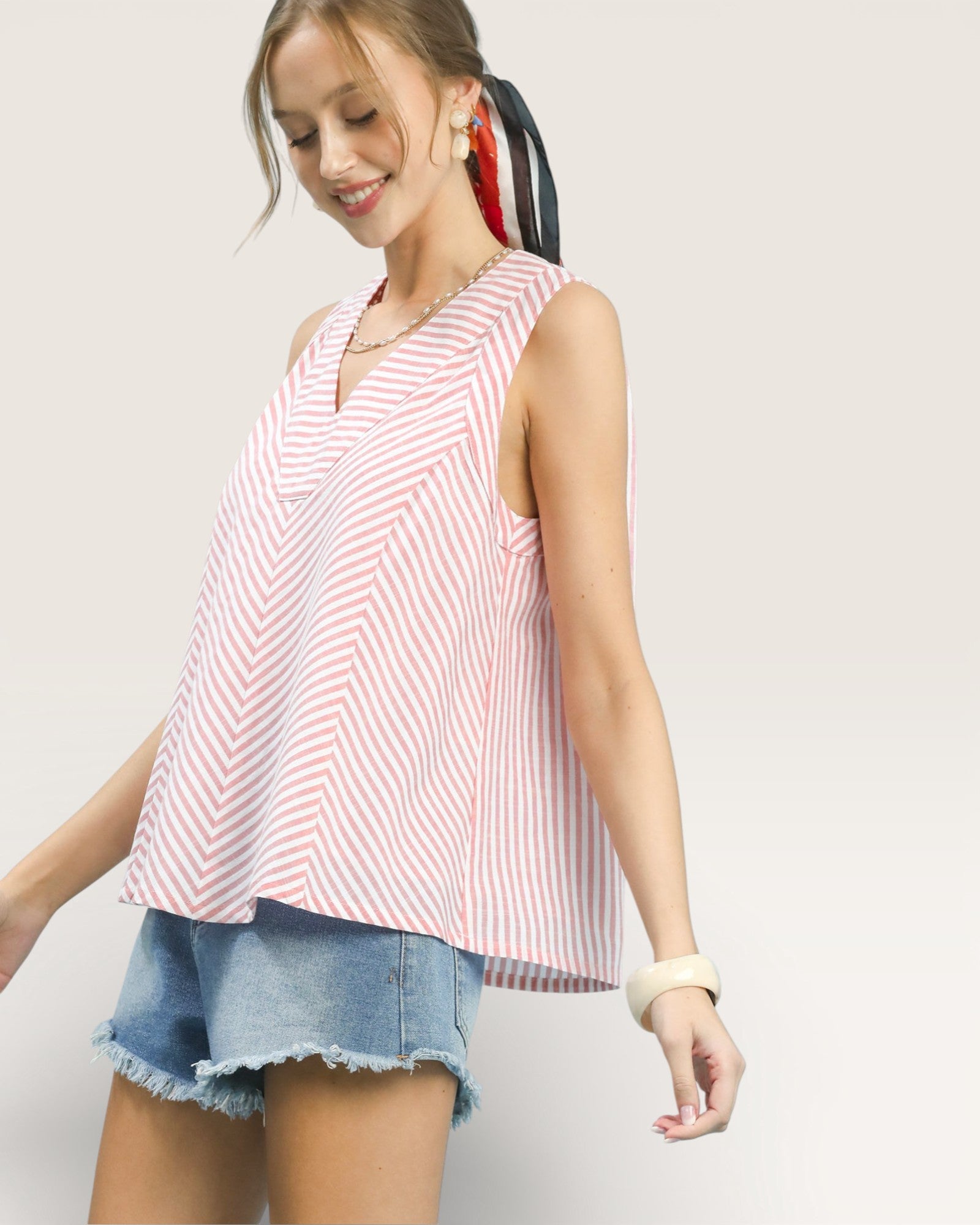 Woman wearing a red and white striped sleeveless top and denim shorts on a light gray background