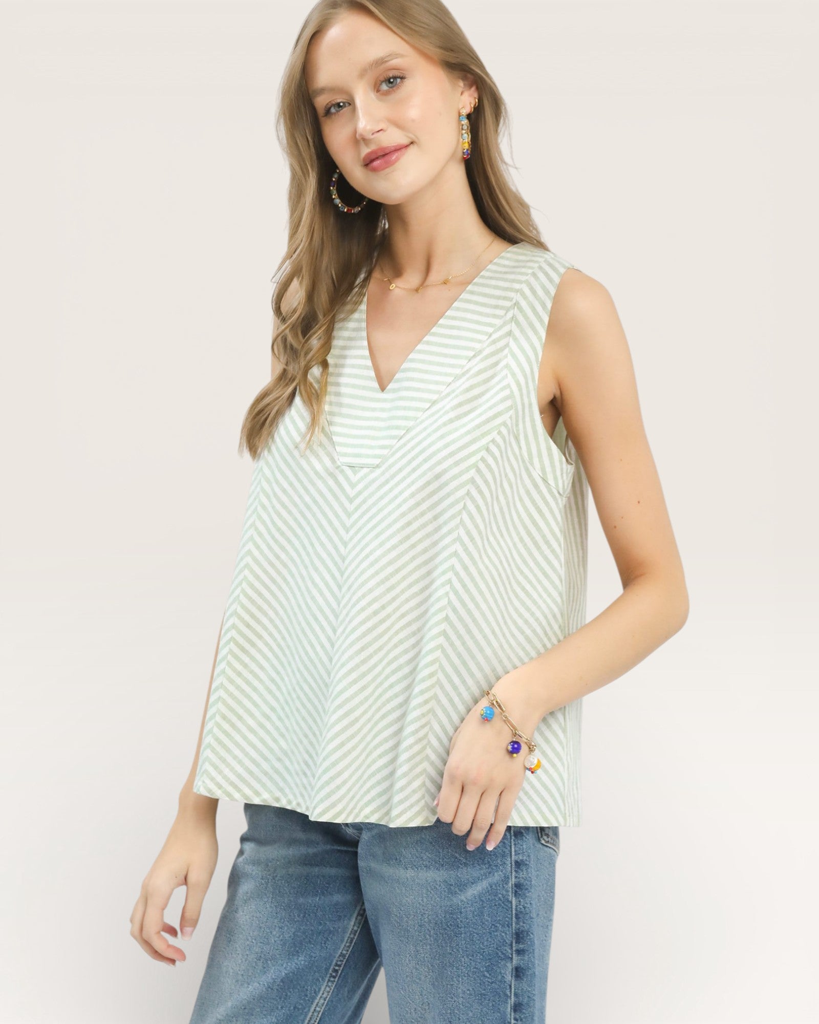 Woman wearing a sleeveless striped top and jeans on a plain background