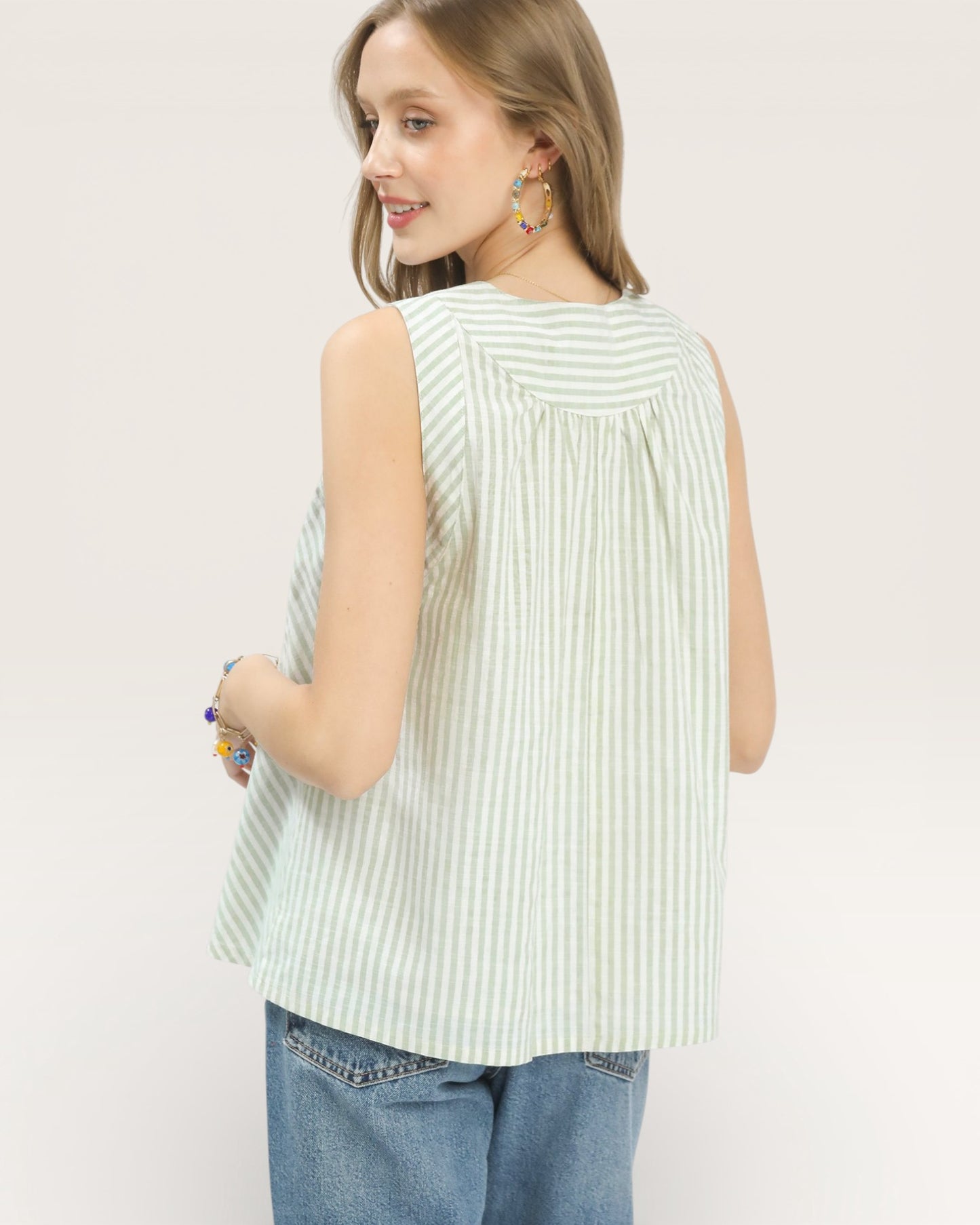 Woman wearing a sleeveless striped top and jeans on a plain background