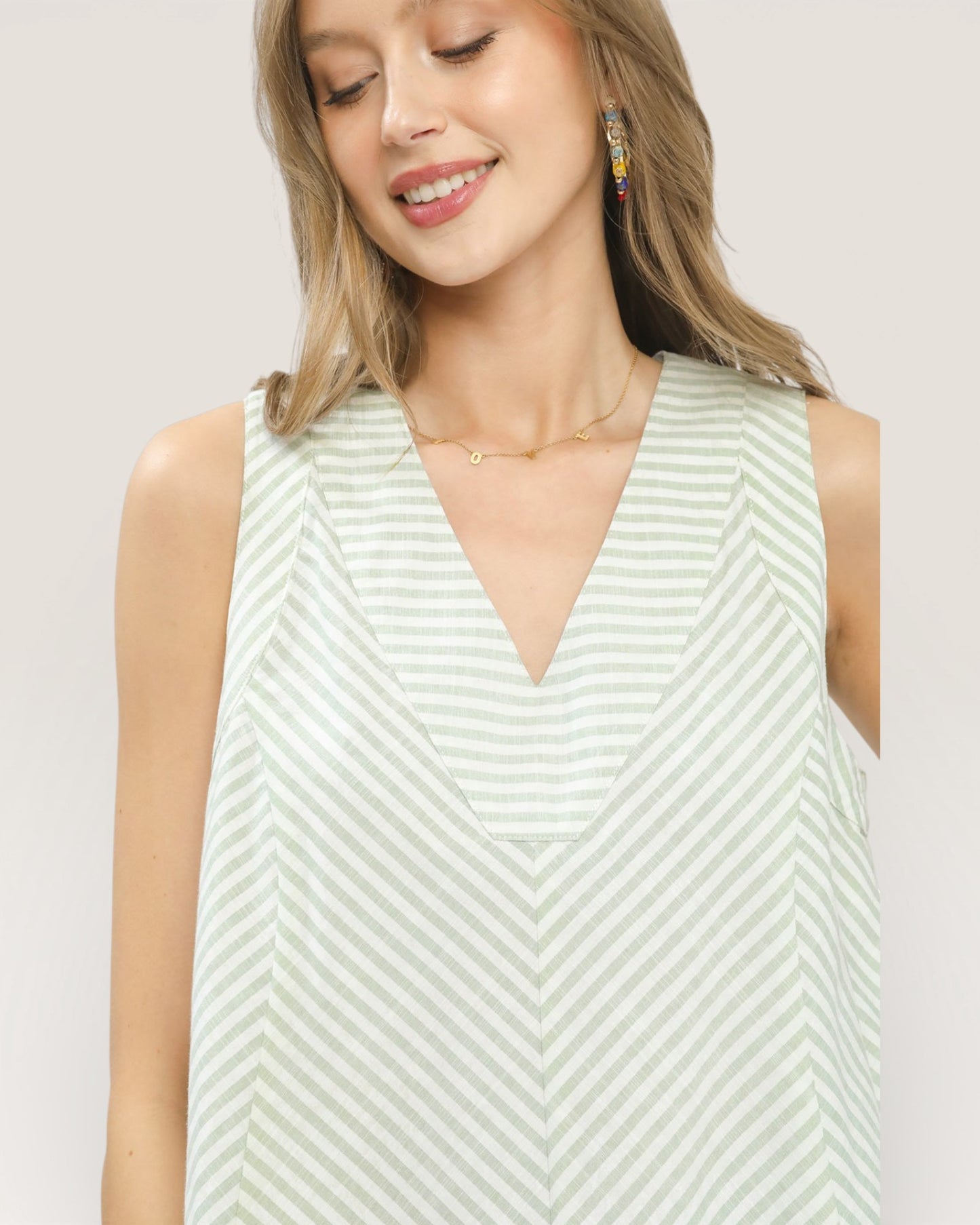 Woman wearing a light green and white striped sleeveless top on a plain background