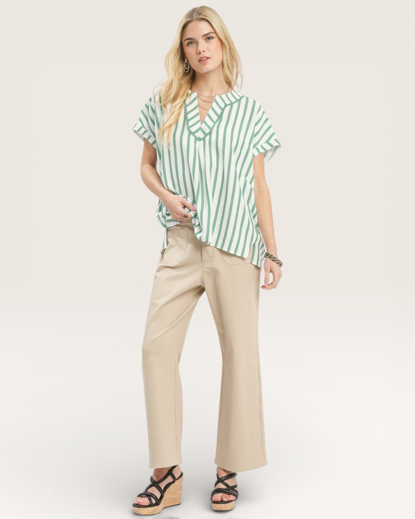 Woman wearing a green and white striped shirt and beige pants on a white background
