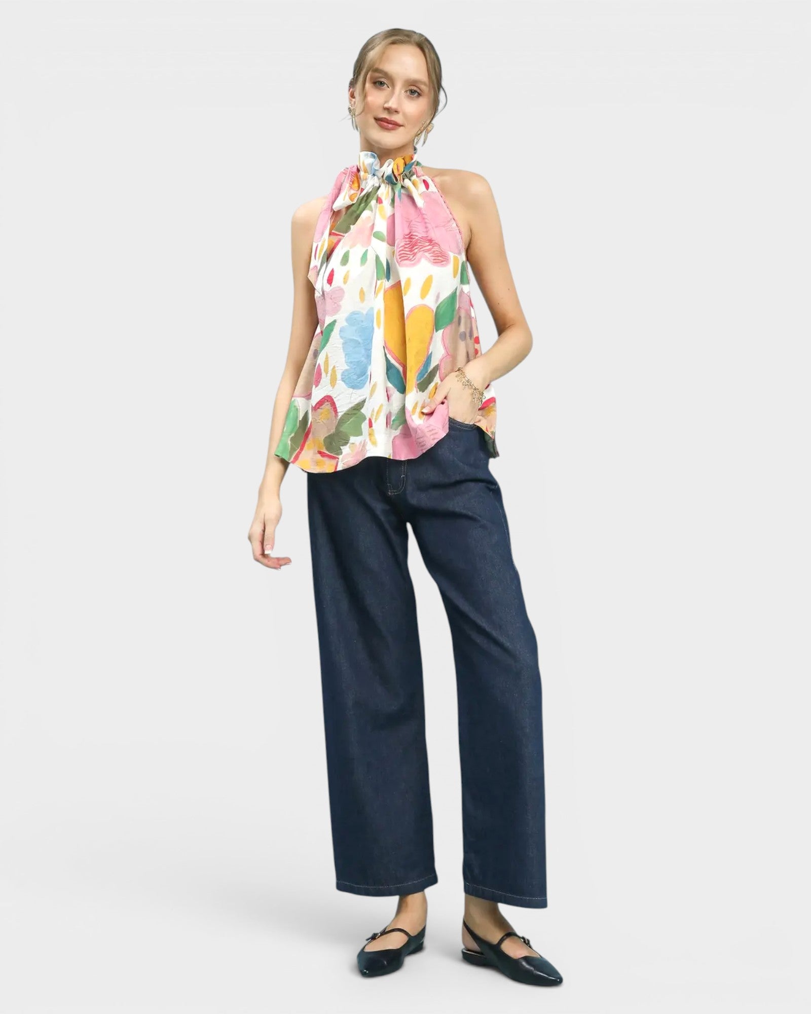 Woman wearing a colorful floral top and dark blue jeans on a white background