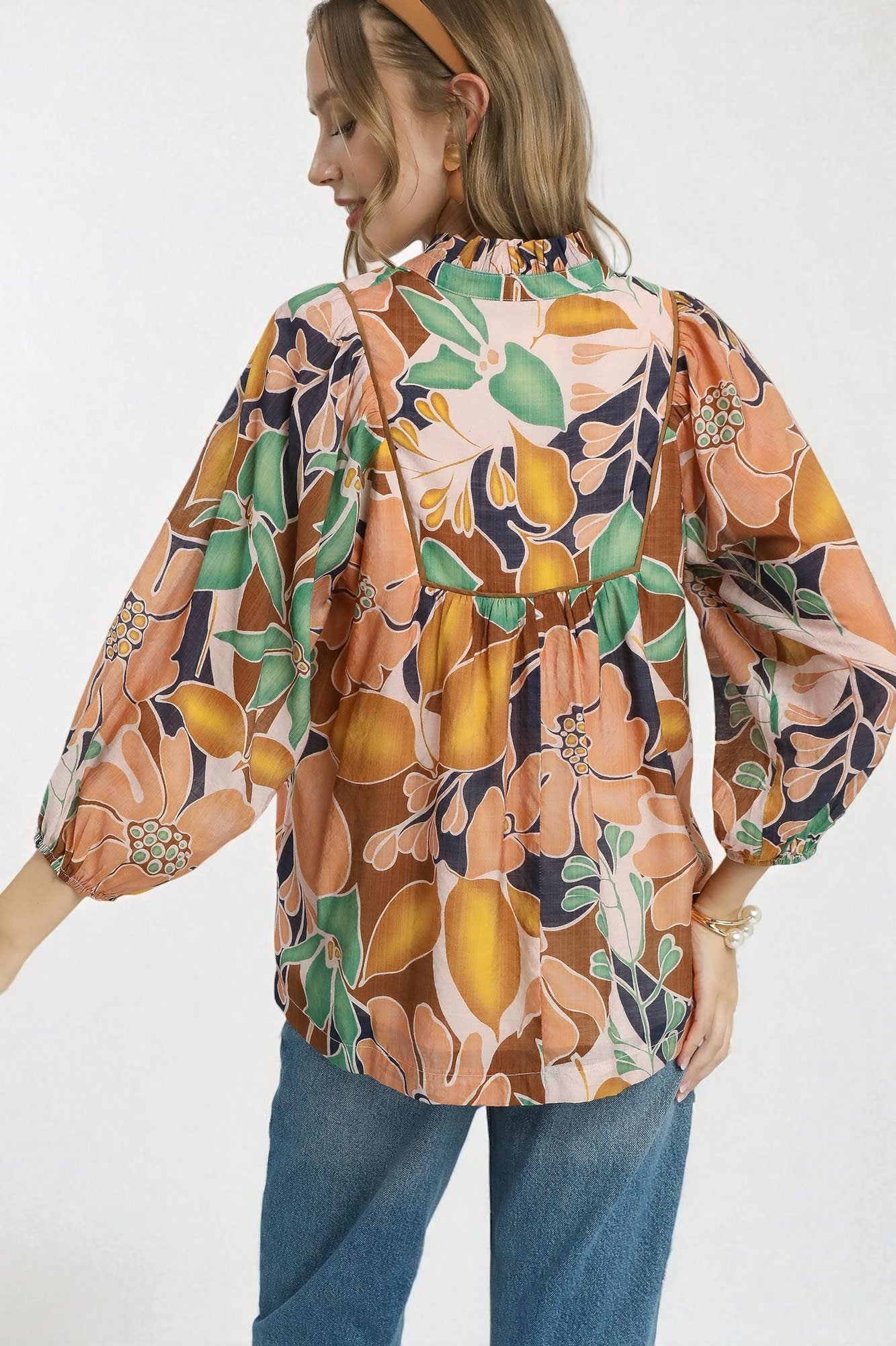 Woman wearing a colorful floral and fruit patterned blouse with blue jeans on a white background