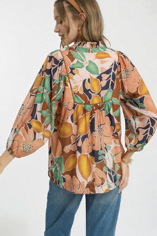 Woman wearing a colorful floral and fruit patterned blouse with blue jeans on a white background