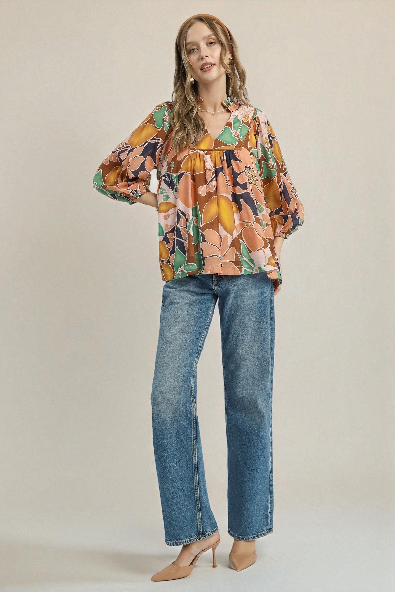 Woman wearing a colorful floral blouse and blue jeans on a beige background