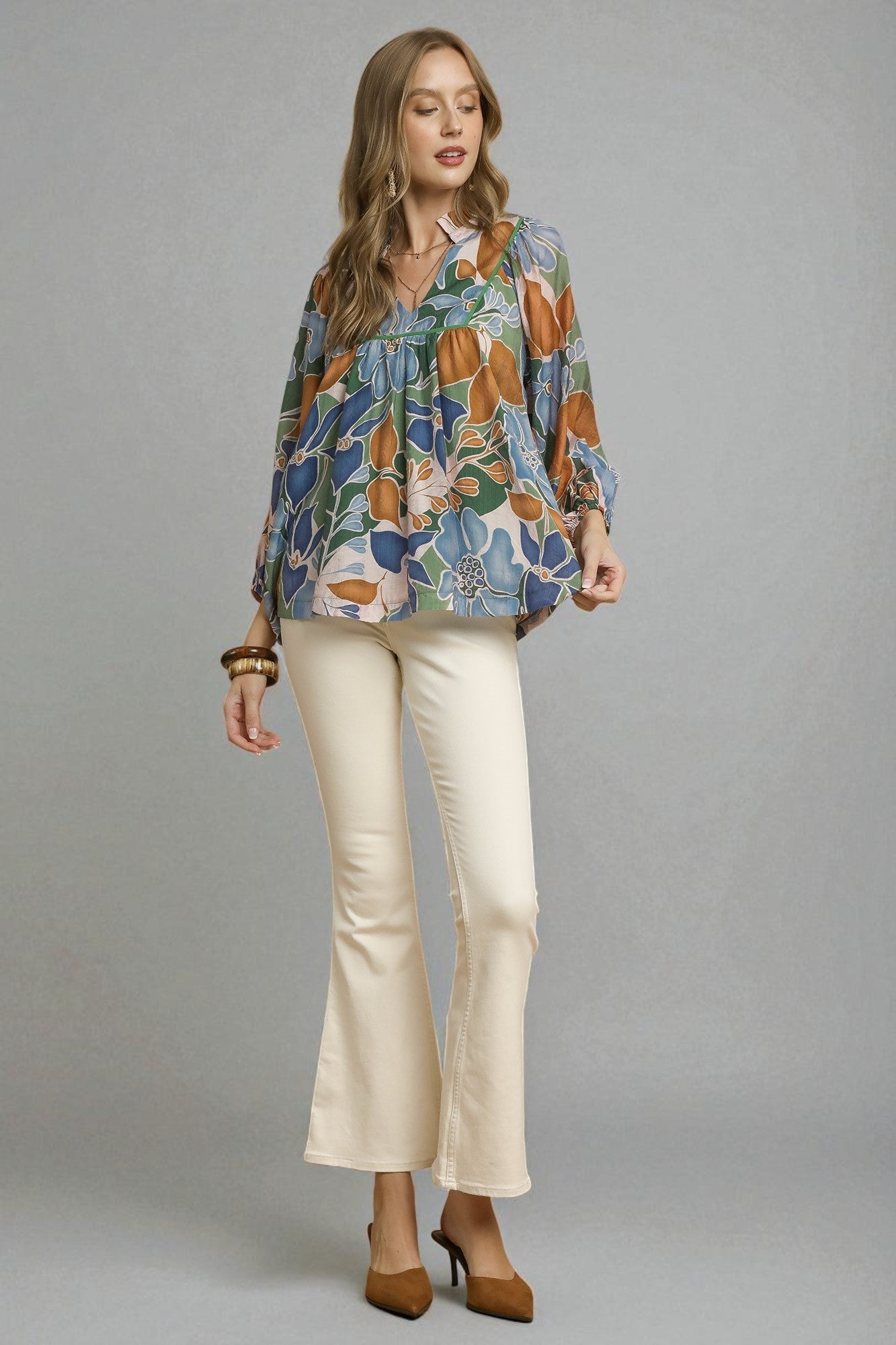Woman wearing a colorful floral blouse and beige pants on a gray background