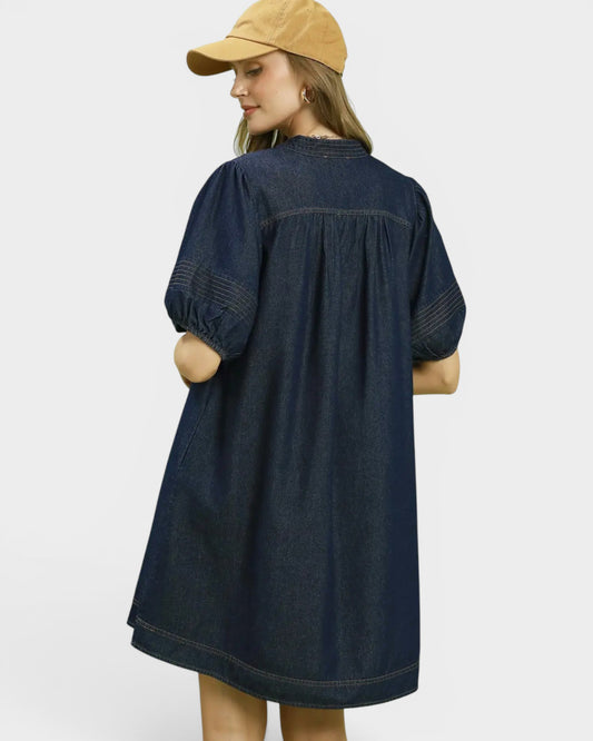 Woman wearing a dark denim dress and beige cap on a white background