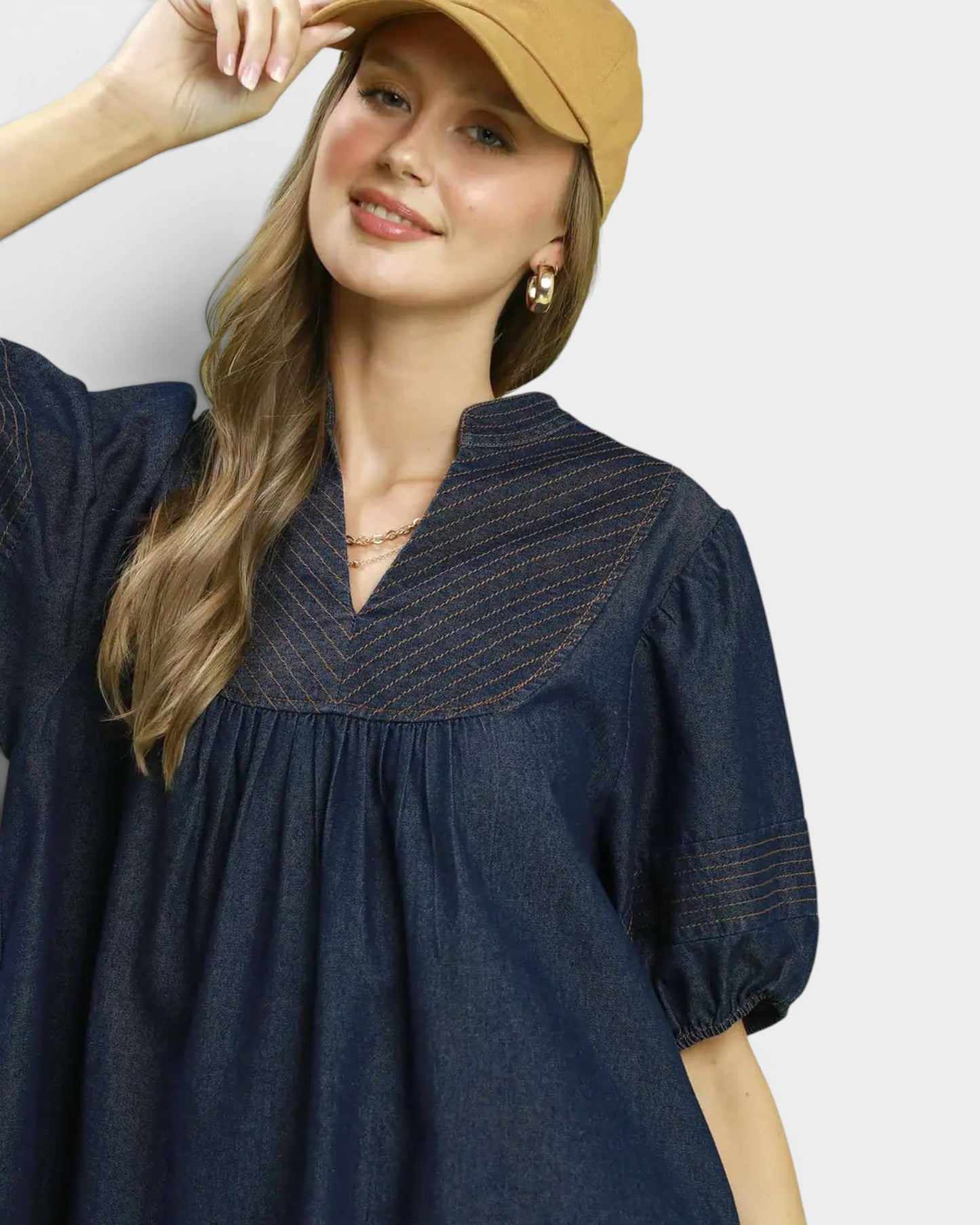 Woman wearing a navy blue dress with a beige cap on a light gray background