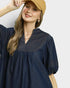 Woman wearing a navy blue dress with a beige cap on a light gray background