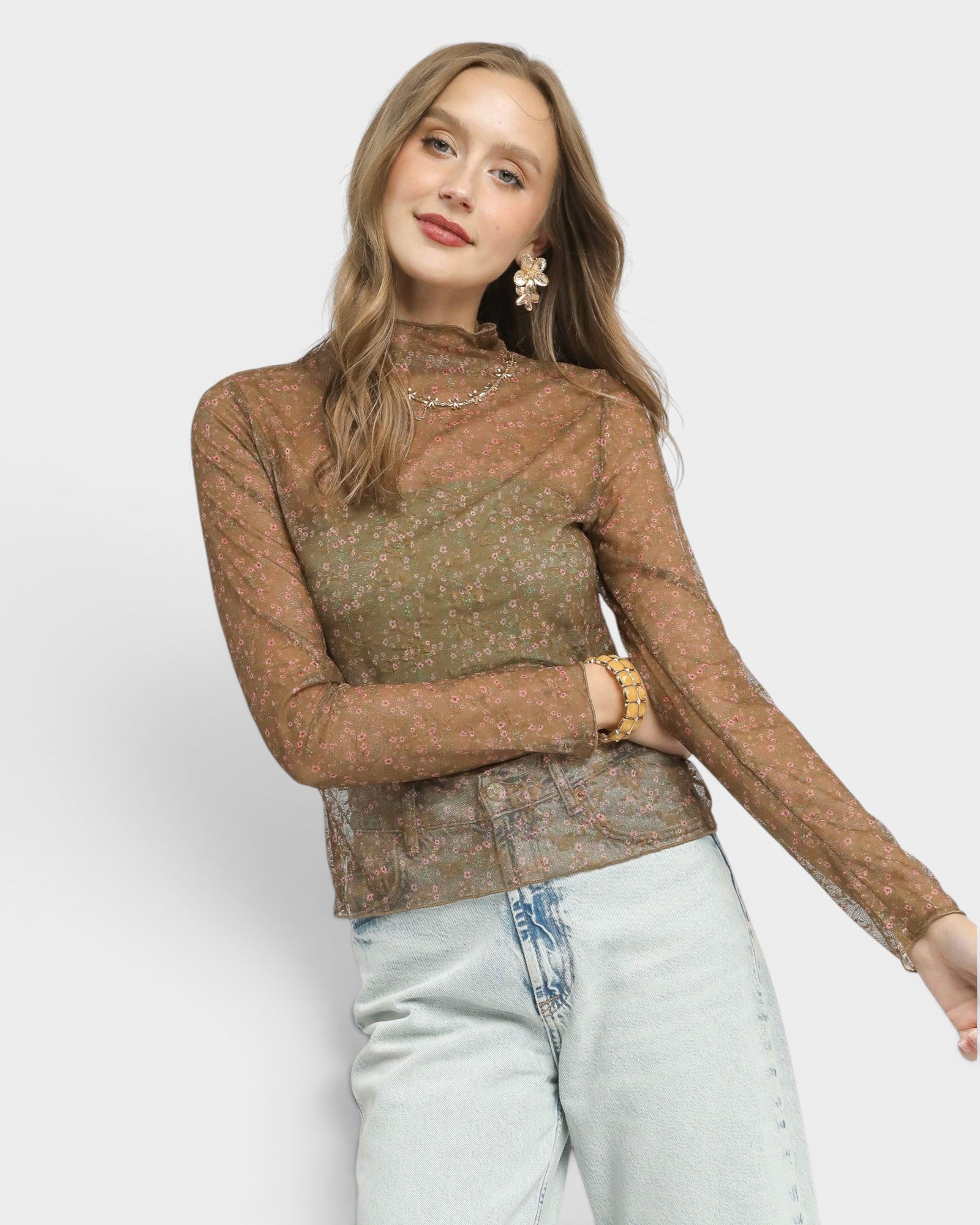 Woman wearing a brown sheer long-sleeve top with a patterned design on a white background