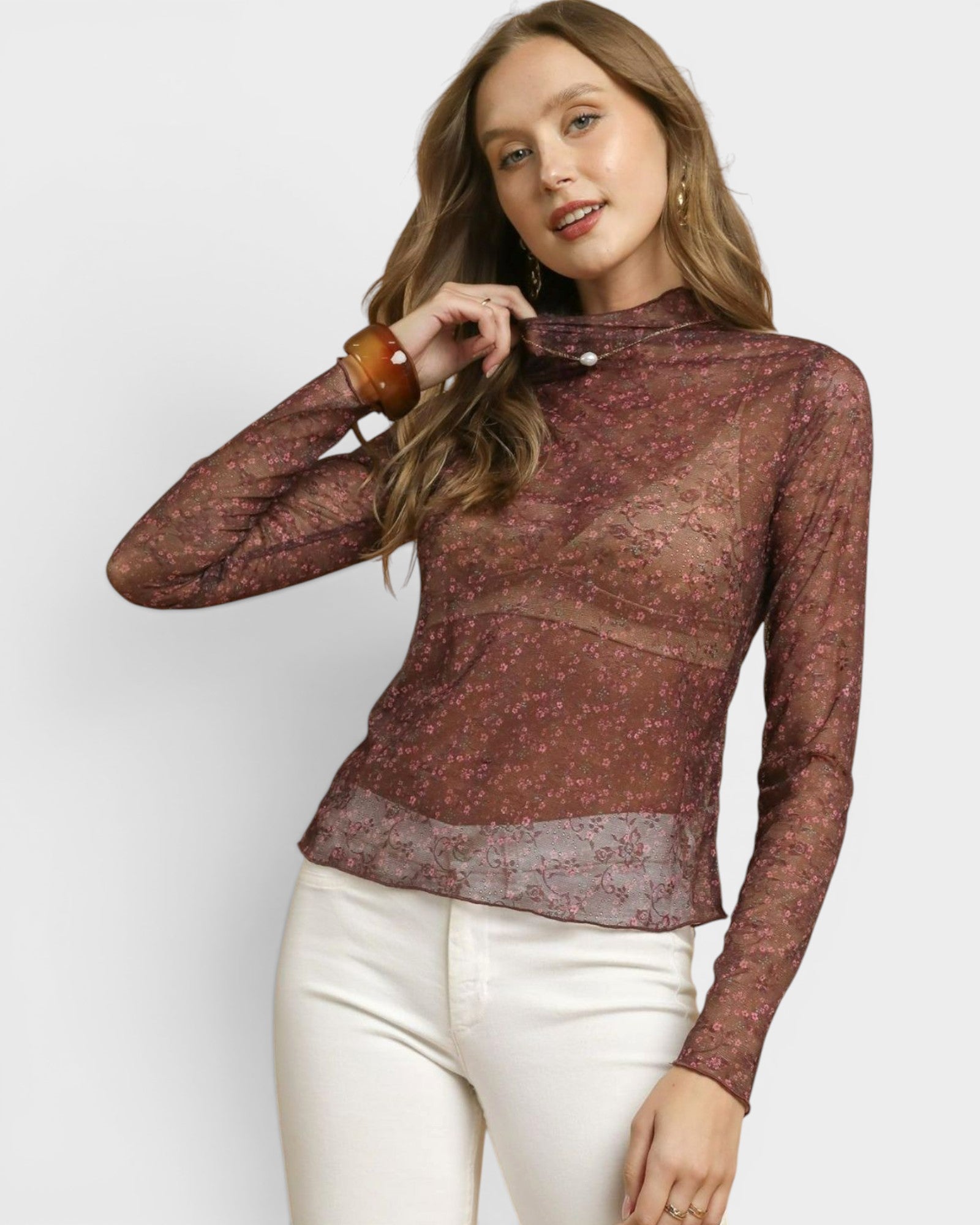 Woman wearing a sheer brown long-sleeve top with white pants on a light gray background