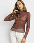Woman wearing a sheer brown long-sleeve top with white pants on a light gray background