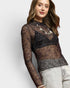 Woman wearing a sheer black lace top with long sleeves on a light gray background