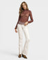 Woman wearing a brown lace top and white pants on a light gray background
