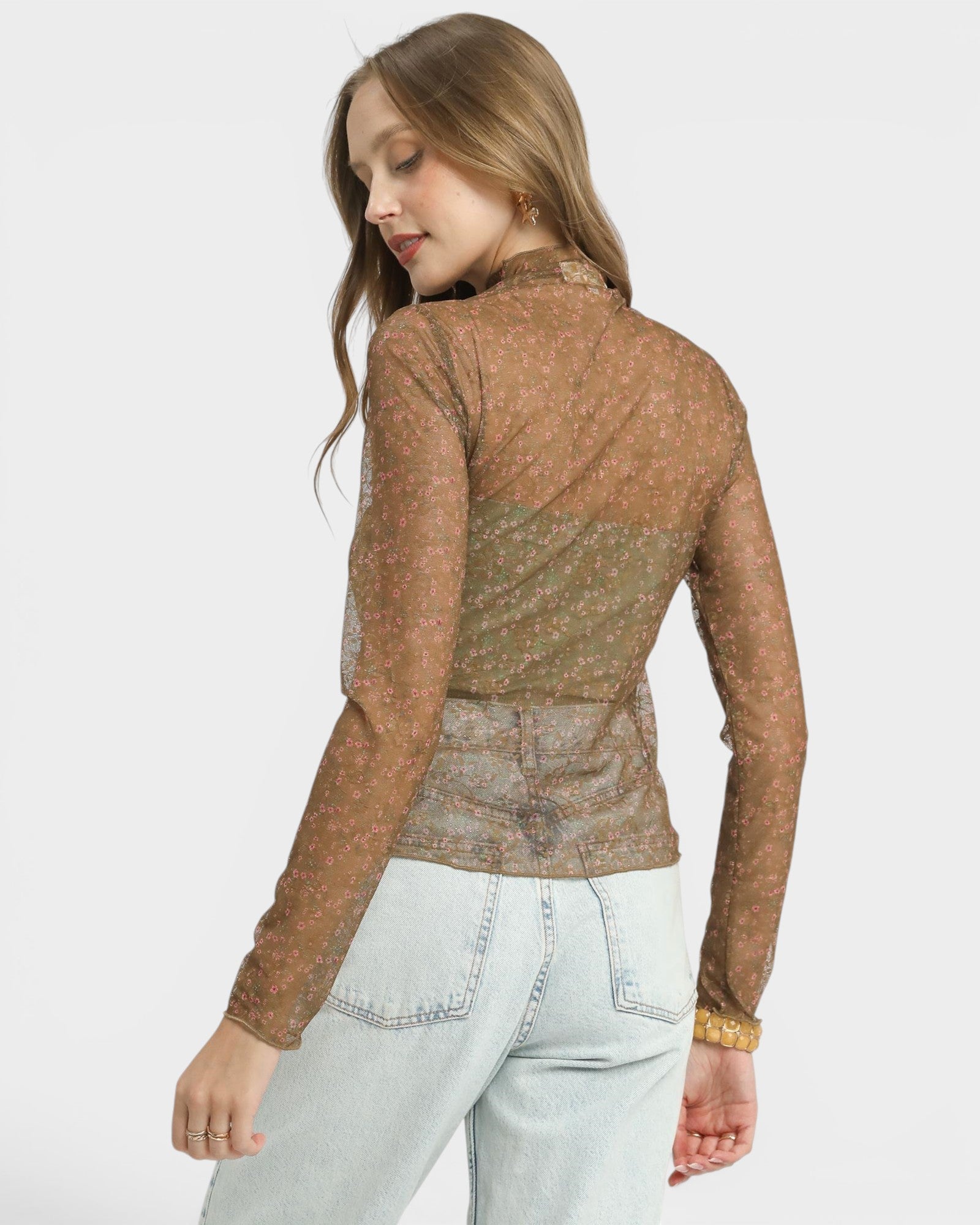 Woman wearing a brown patterned jacket and light blue jeans on a white background